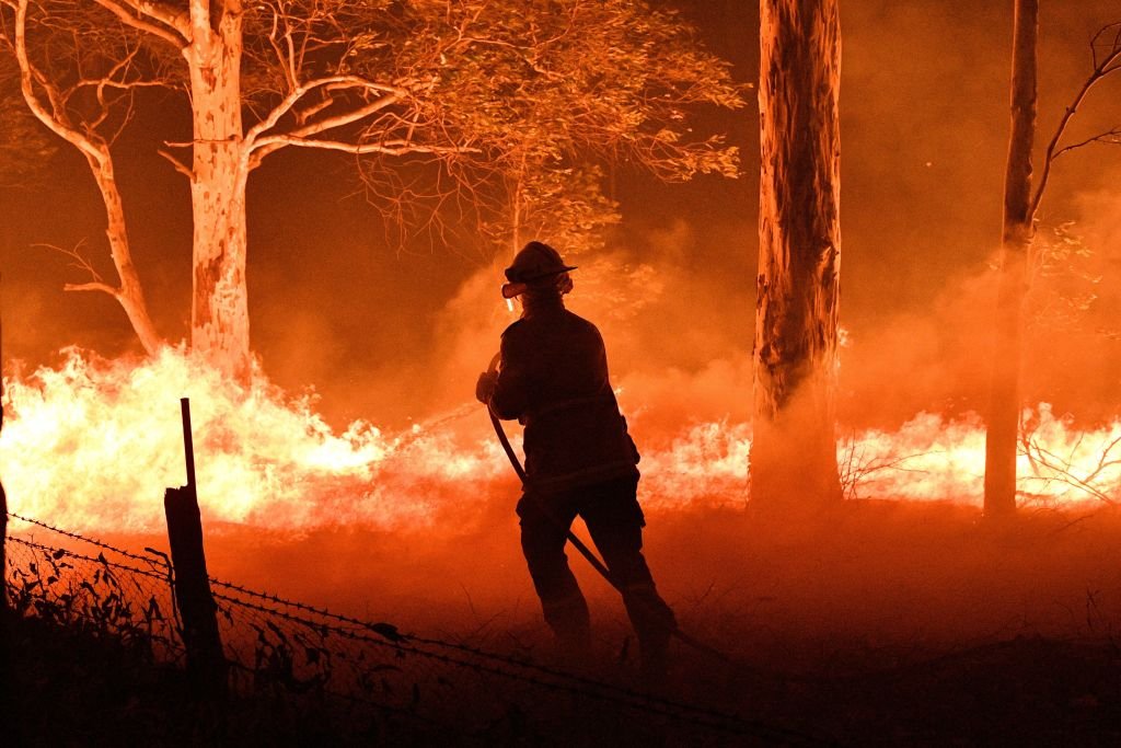 TOPSHOT - This picture taken on December 31, 2019 shows a firefighter hosing down trees and flying embers in an effort to secure nearby houses from bushfires near the town of Nowra in the Australian state of New South Wales. - Fire-ravaged Australia has launched a major operation to reach thousands of people stranded in seaside towns after deadly bushfires ripped through popular tourist areas on New Year's Eve. (Photo by SAEED KHAN / AFP) (Photo by SAEED KHAN/AFP via Getty Images)