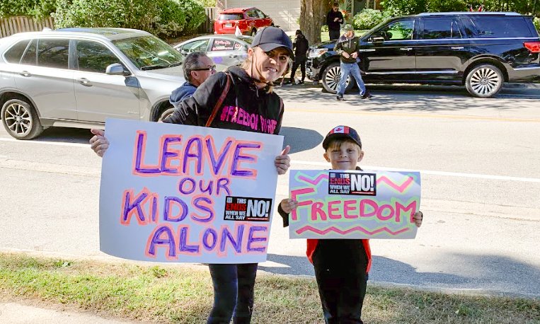 A local mother and her child protest outside Oakville Trafalgar High School on Sept. 23. against a teacher wearing large prosthetic breasts to class. (Peter Wilson/The Epoch Times)
