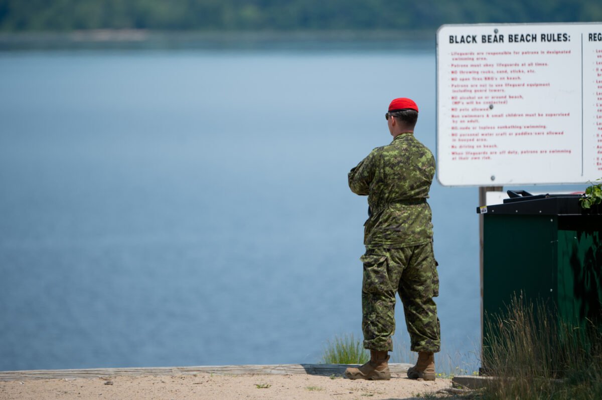 A Canadian Forces Military Police officer watches the water on Black Bear Beach near Garrison Petawawa in Petawawa, Ont. on June 20, 2023. The Royal Canadian Air Force is currently searching for two missing RCAF 450 Tactical Helicopter Squadron members following a CH-147F Chinook early morning crash near Garrison Petawawa. (THE CANADIAN PRESS/Spencer Colby)