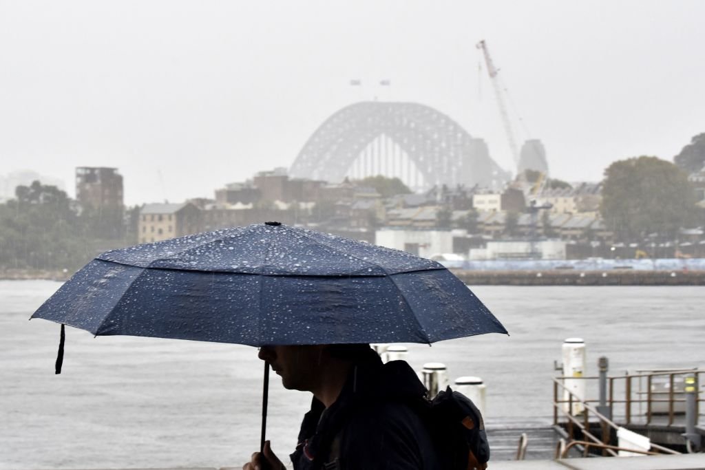 A man walks in front of the Harbour Bridge during rainfall in Sydney on April 7, 2022, as inclement weather triggered evacuation orders in several suburbs of Sydney's south and southwest. (Photo by Muhammad Farooq/AFP via Getty Images)