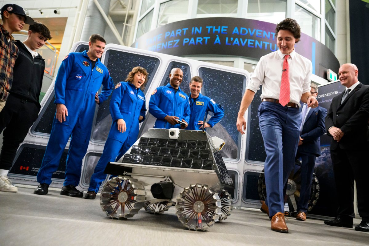 Prime Minister Justin Trudeau tries to see if the remote-controlled lunar rover being tested out by NASA astronaut Victor Glover (C) will run over his foot or stop automatically, as he meets with the crew of the Artemis II at the Canada Aviation and Space Museum in Ottawa on April 25, 2023. (The Canadian Press/Justin Tang)