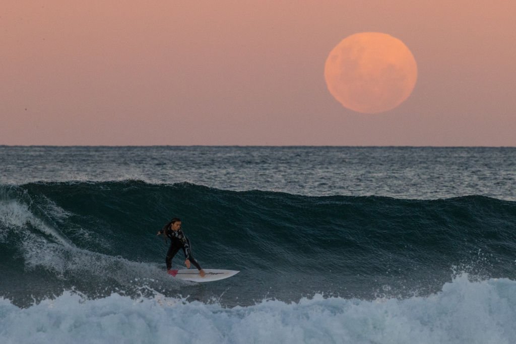 A surfer rides a wave as a super blood moon rises above the horizon at Manly Beach in Sydney, Australia, on May 26, 2021. (Cameron Spencer/Getty Images)